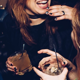 A woman laughing and socializing over drinks with a friend